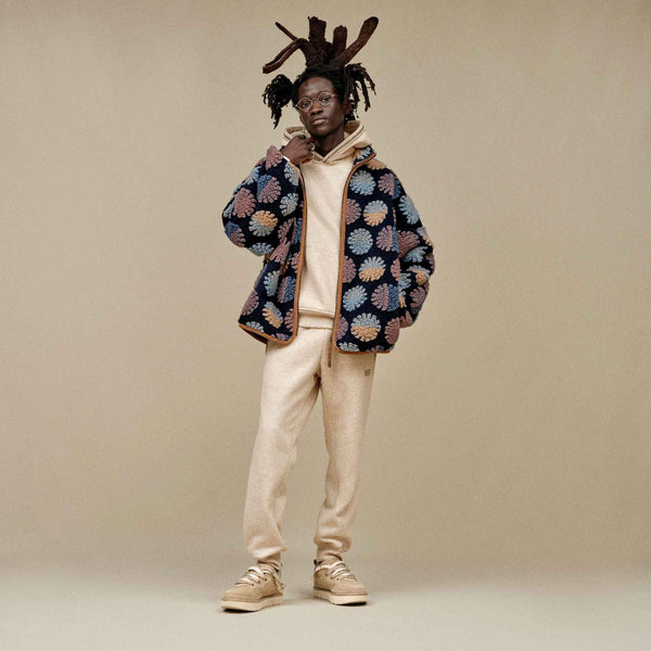 Person wearing a patterned jacket and beige pants on a plain background