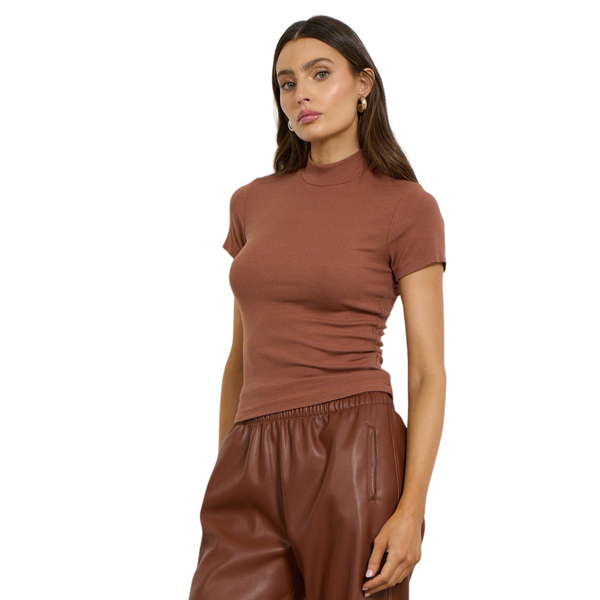 Woman in a brown T-shirt and brown leather pants, with her hand by her side.