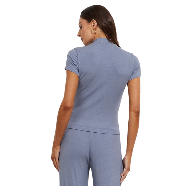 Woman in a blue shirt and pants, viewed from behind, standing against a white background.