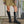 Person in a khaki skirt and black knee-high boots standing on a pavement.